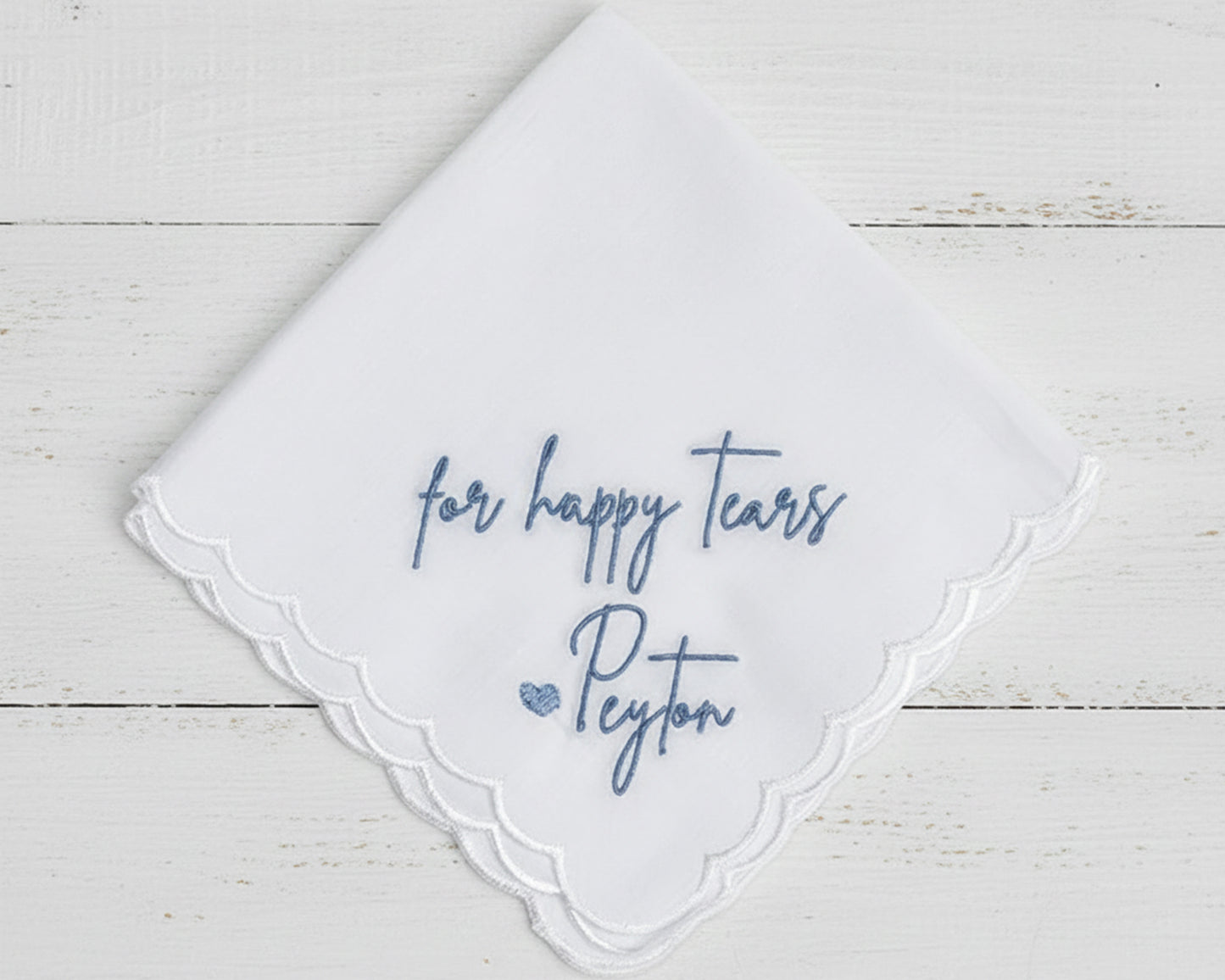 A white cotton-blend bridal handkerchief with a scalloped edge featuring blue "for happy tears" and "Peyton" script embroidery.