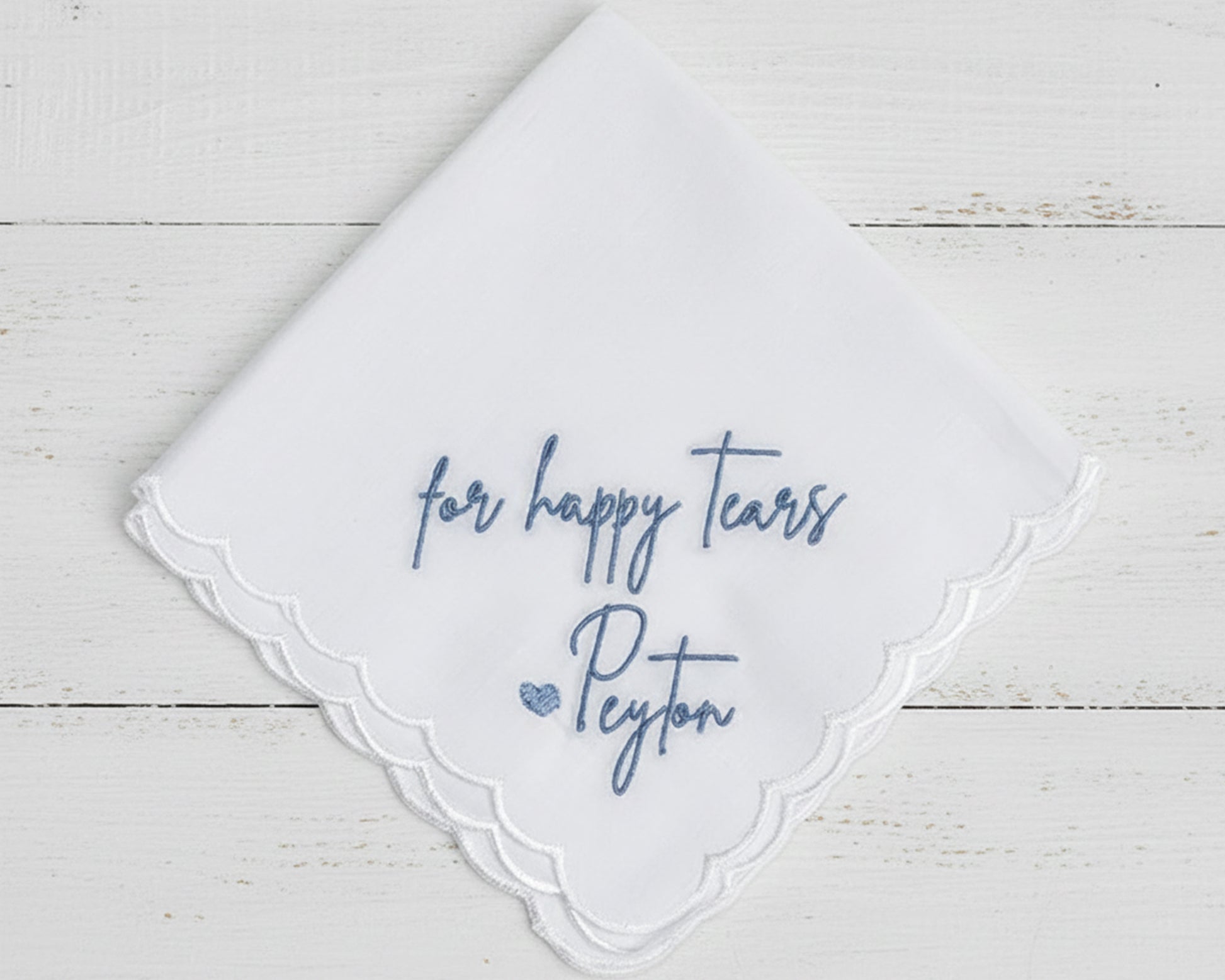A white cotton-blend bridal handkerchief with a scalloped edge featuring blue "for happy tears" and "Peyton" script embroidery.