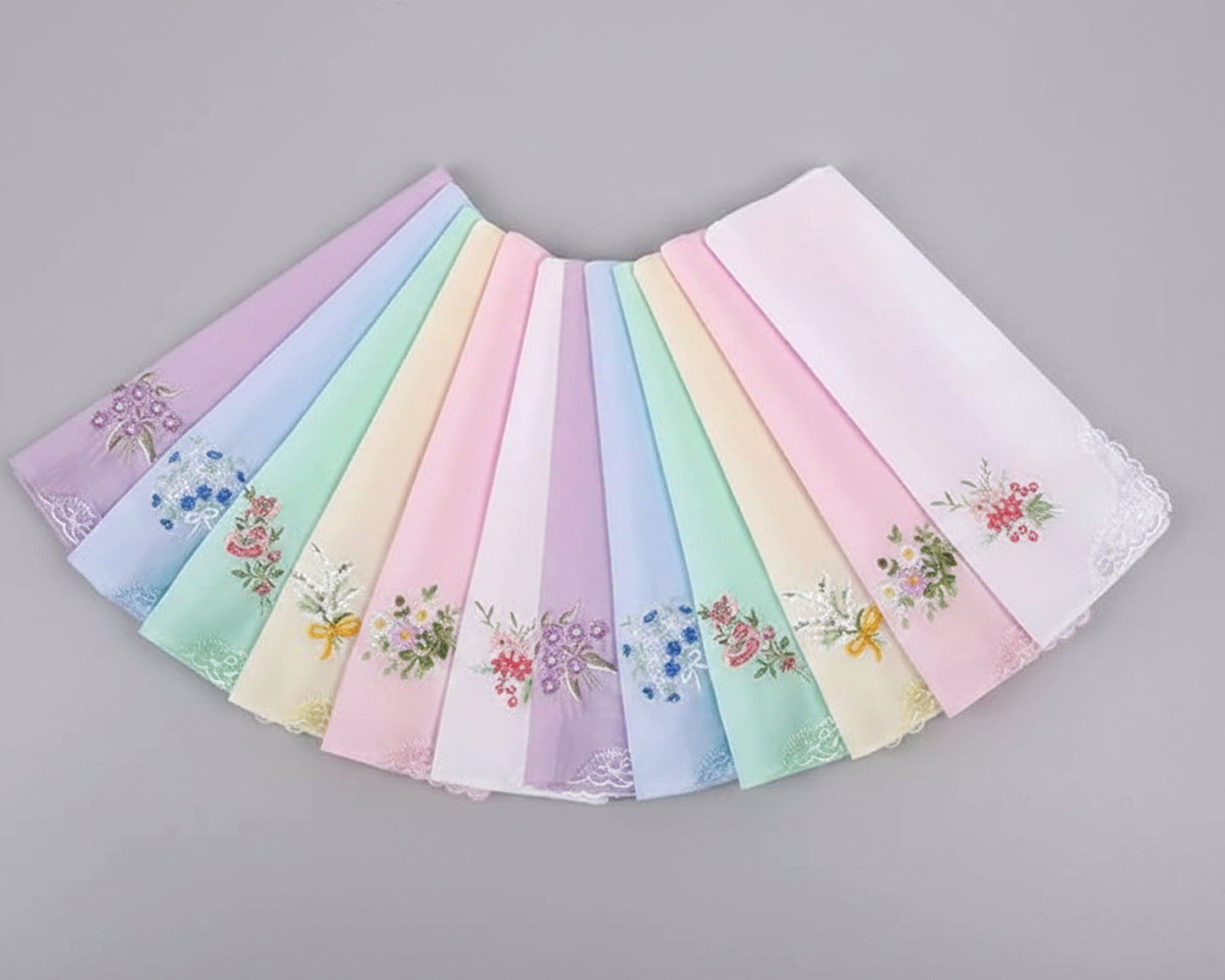 Three pink cotton handkerchiefs with butterfly lace corners and central floral embroidery on a white wood background