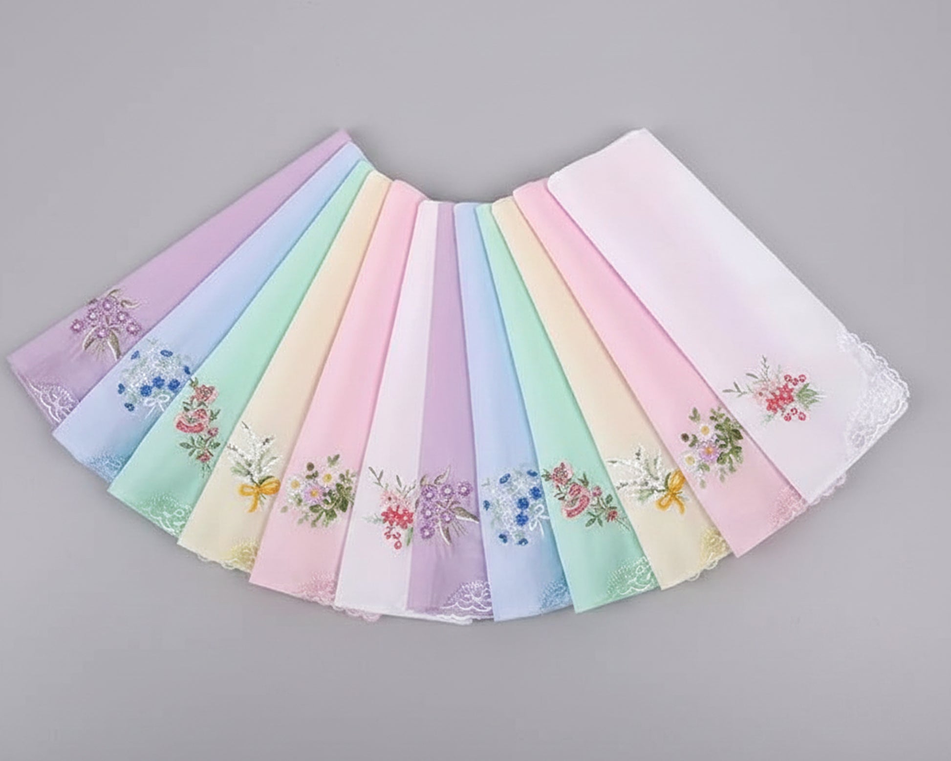 Three pink cotton handkerchiefs with butterfly lace corners and central floral embroidery on a white wood background