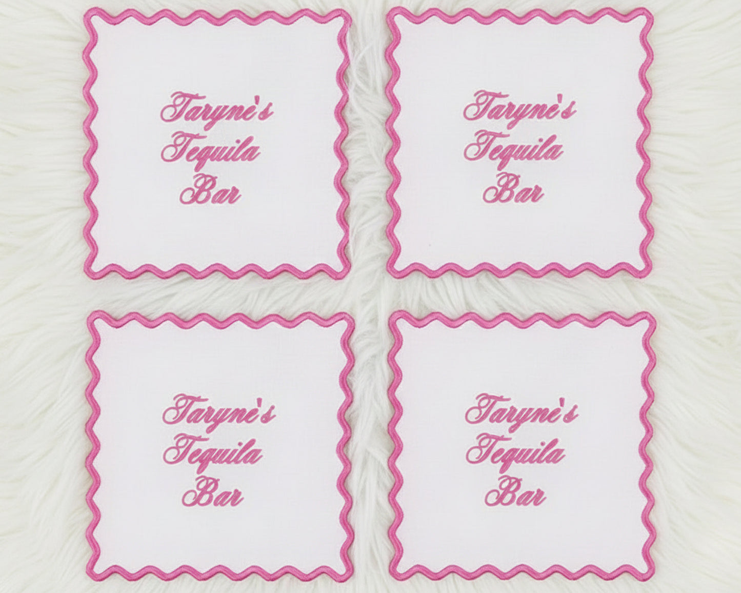 A set of four white linen cocktail napkins with vibrant pink scalloped borders and "Taryne's Tequila Bar" custom text.