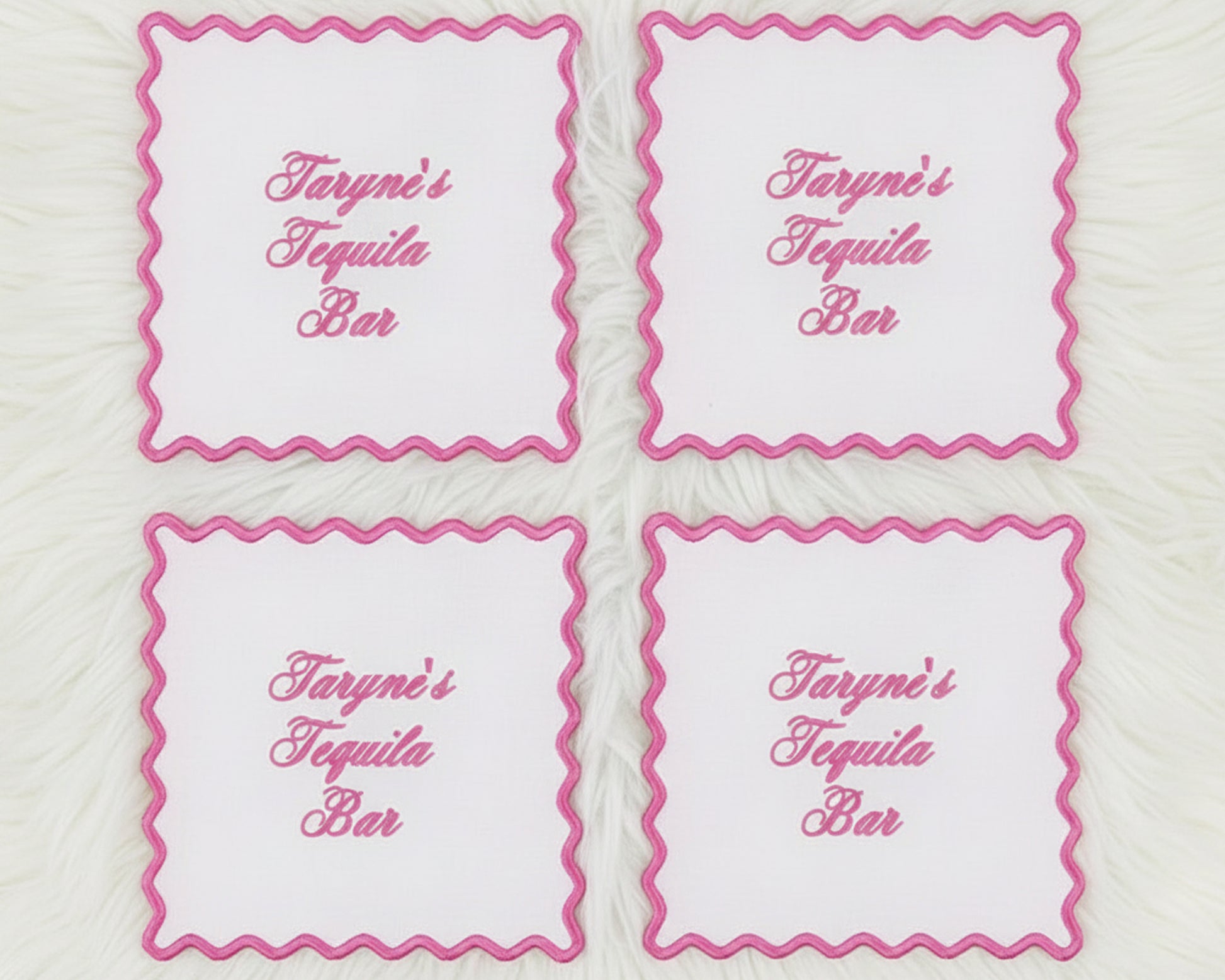 A set of four white linen cocktail napkins with vibrant pink scalloped borders and "Taryne's Tequila Bar" custom text.