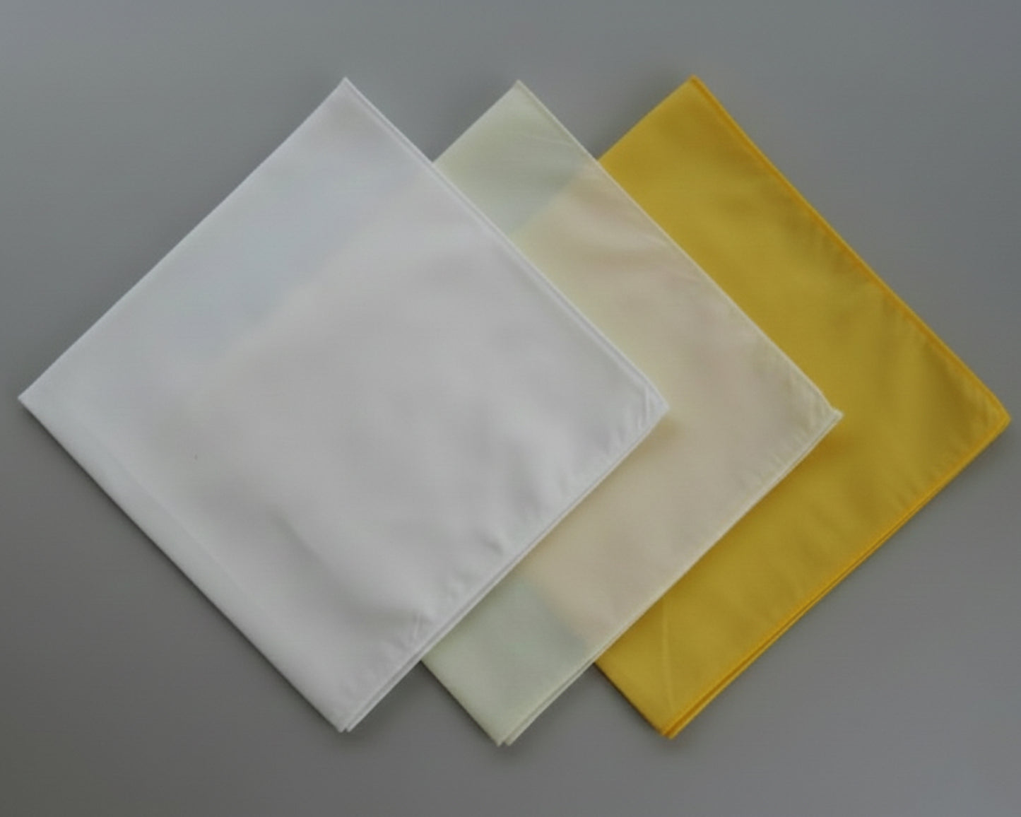 Three square cloths in white, beige, and yellow on a gray background