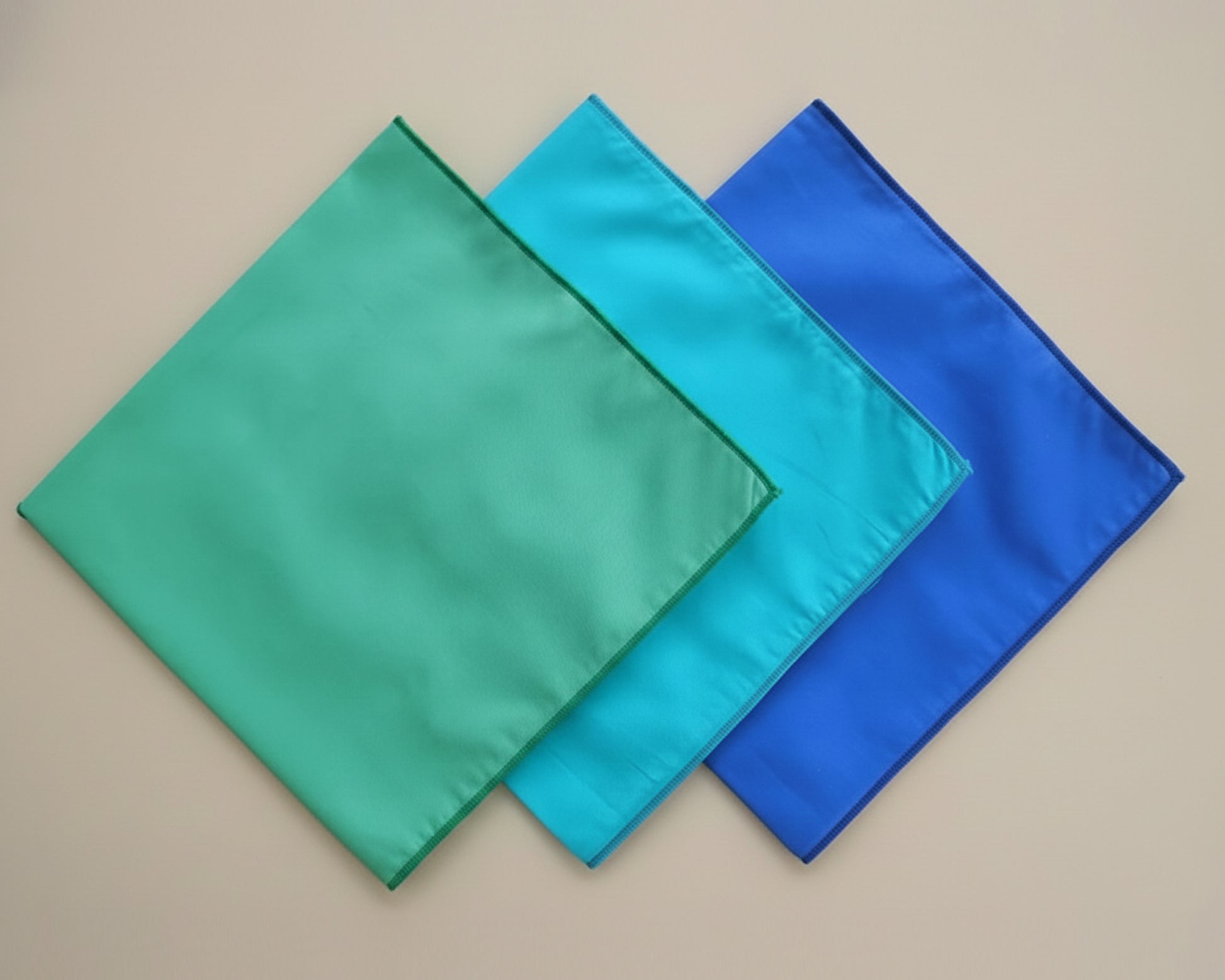Three square cloths in green, blue, and turquoise on a beige background