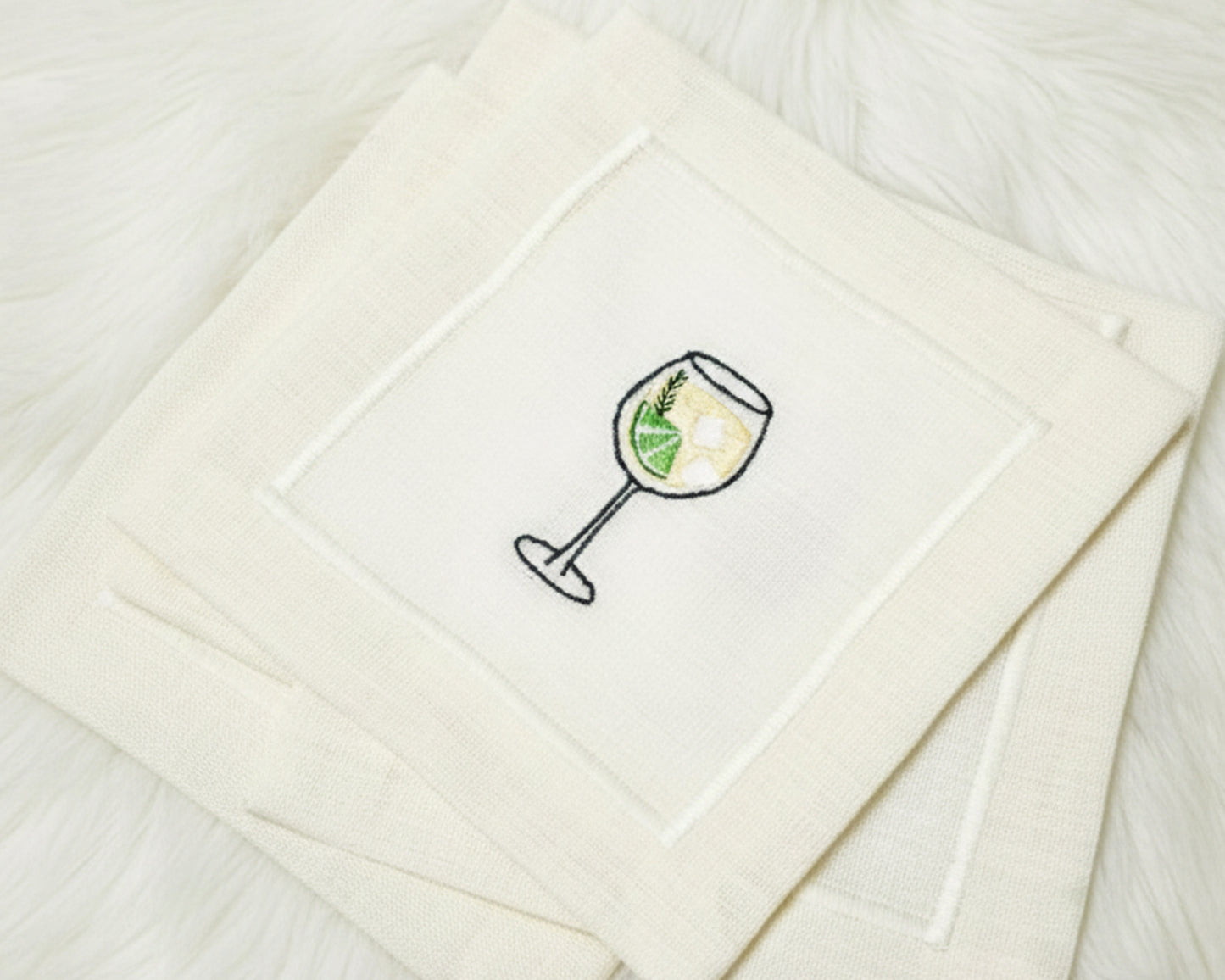 Top-down view of four cotton napkins on a dark marble surface showcasing white wine, Old Fashioned, Gin and Tonic, and Margarita designs.