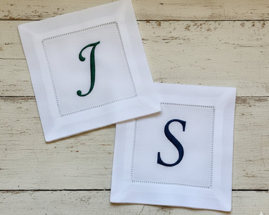 Two white napkins with embroidered letters 'J' and 'S' on a wooden surface.