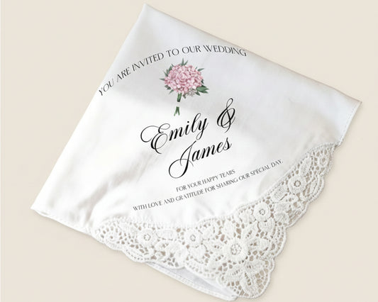 White handkerchief with lace edge, floral design, and wedding invitation text on a beige background.