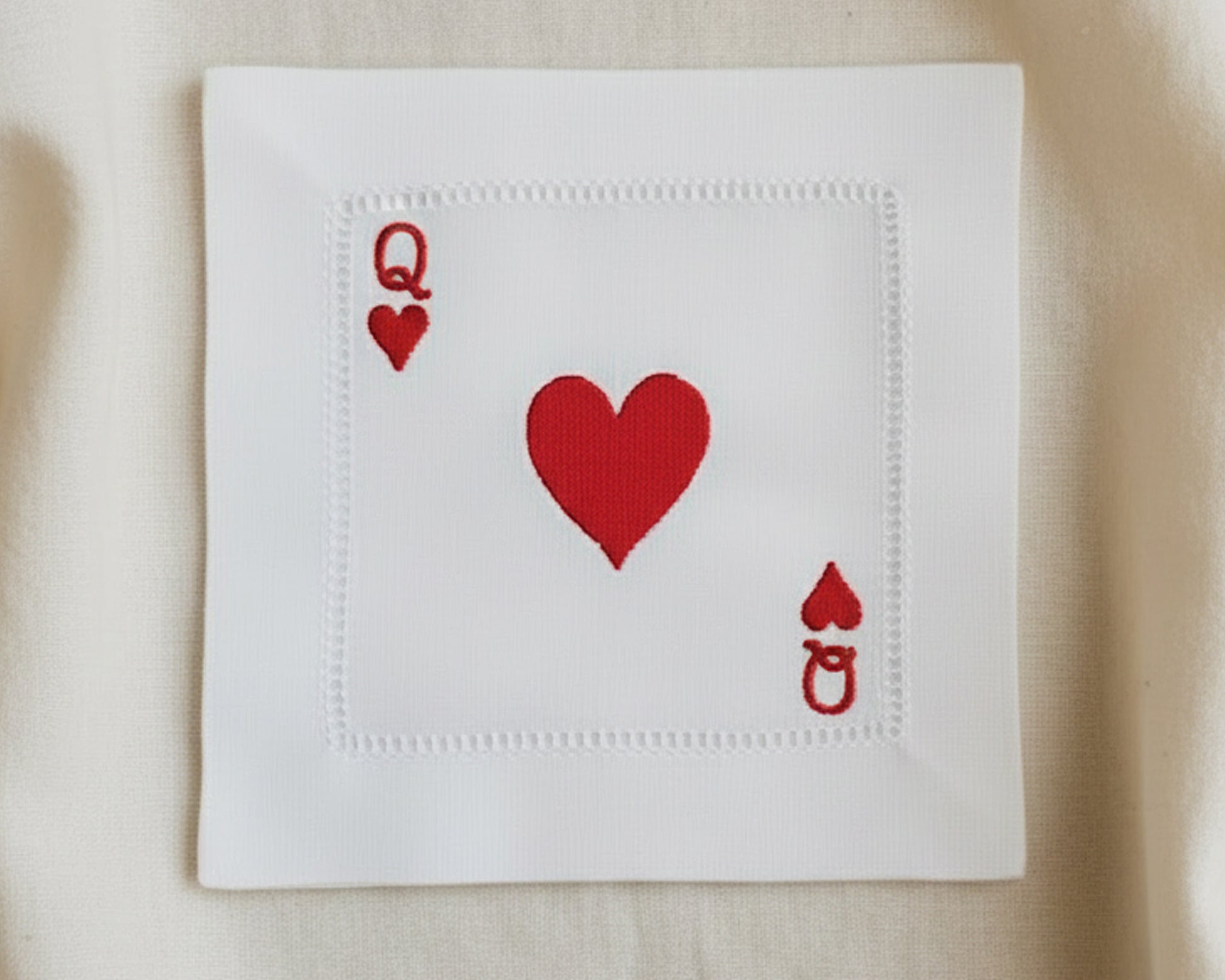 A full set of four white cotton hemstitch napkins featuring the Ace, King, Queen, and Jack of Hearts arranged on a soft silk background.