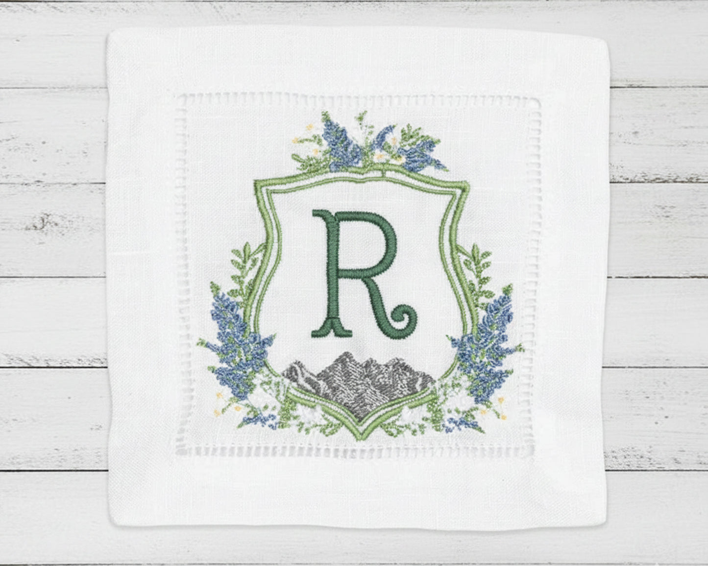 Close-up of a personalized white dinner napkin with a modern sage green 'AR' monogram