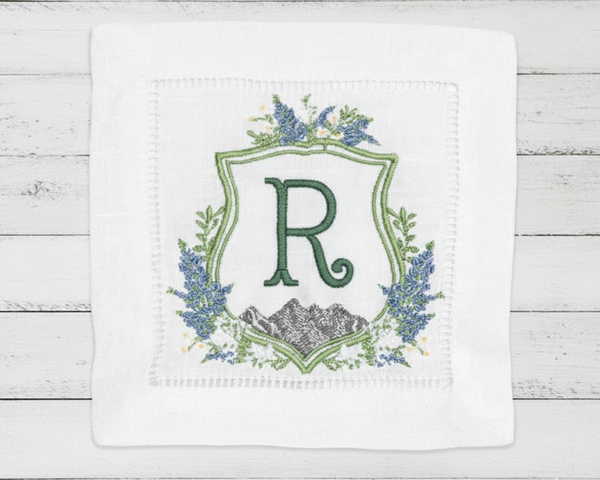 Close-up of a personalized white dinner napkin with a modern sage green 'AR' monogram