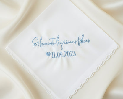 A customized 100% cotton handkerchief featuring the Spanish sentiment for happy tears and a wedding date, placed on a rustic dark wood surface.