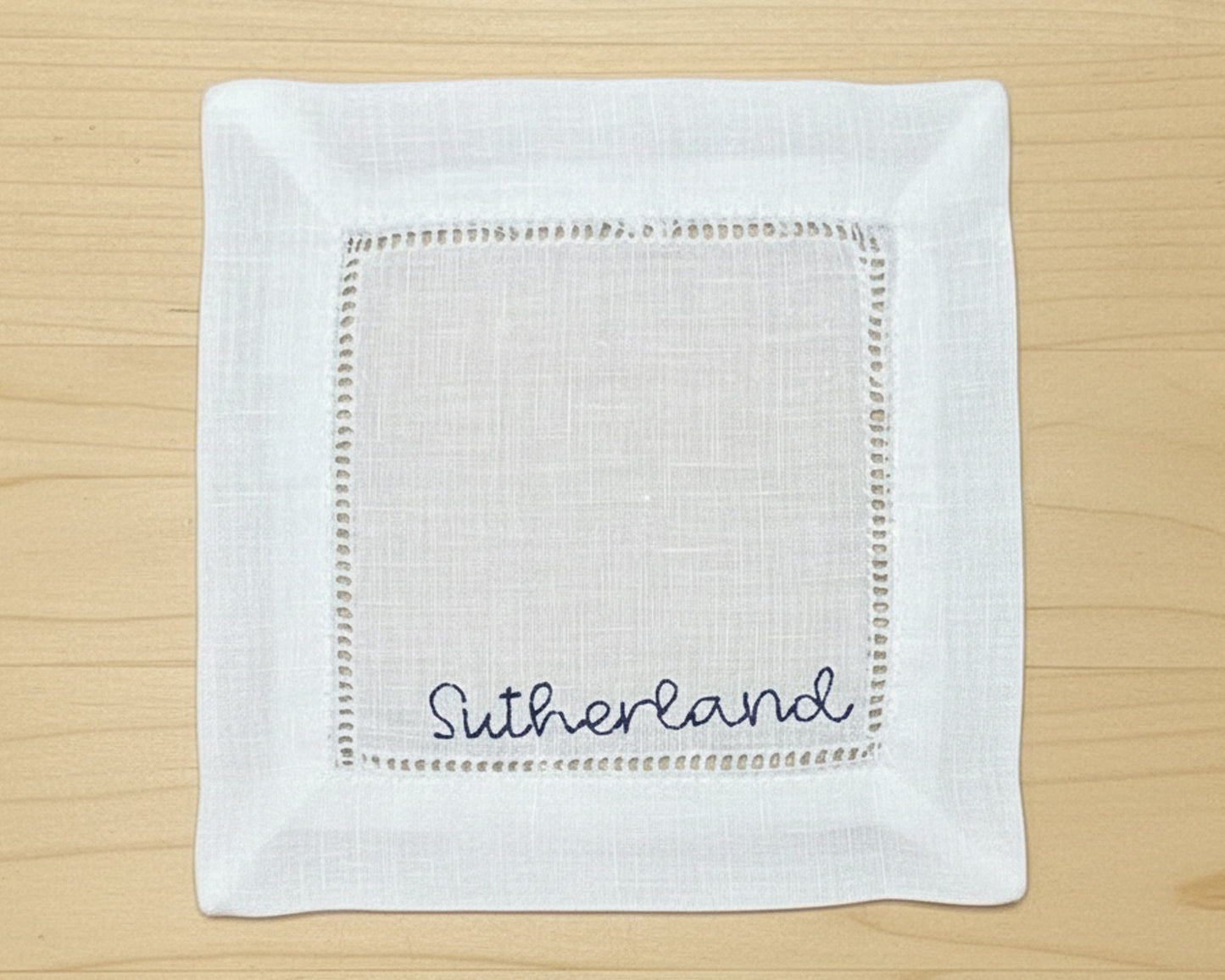 A close-up of a white cotton hemstitch napkin featuring a sophisticated sky blue embroidered letter "B" in a classic serif font.