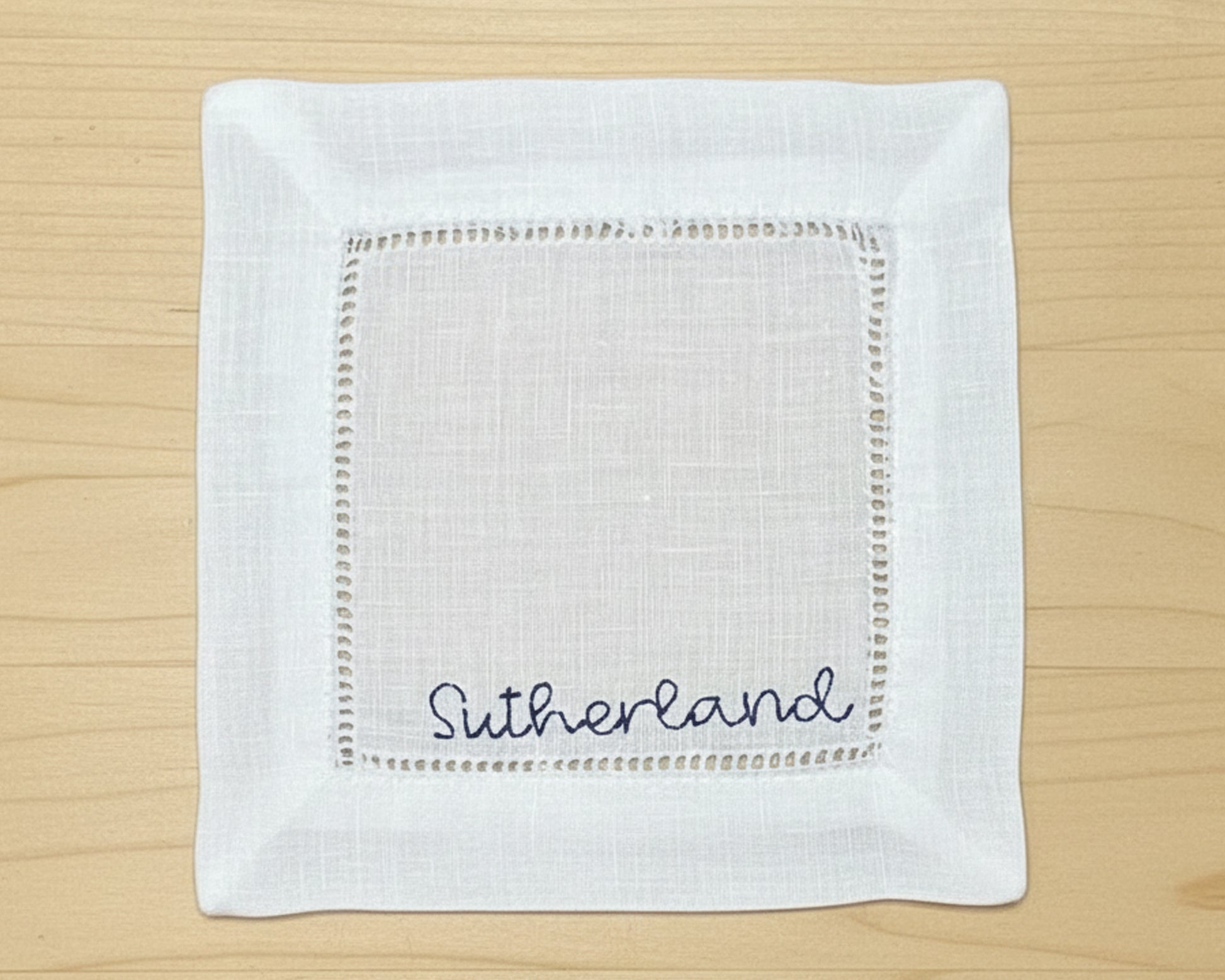 A close-up of a white cotton hemstitch napkin featuring a sophisticated sky blue embroidered letter "B" in a classic serif font.