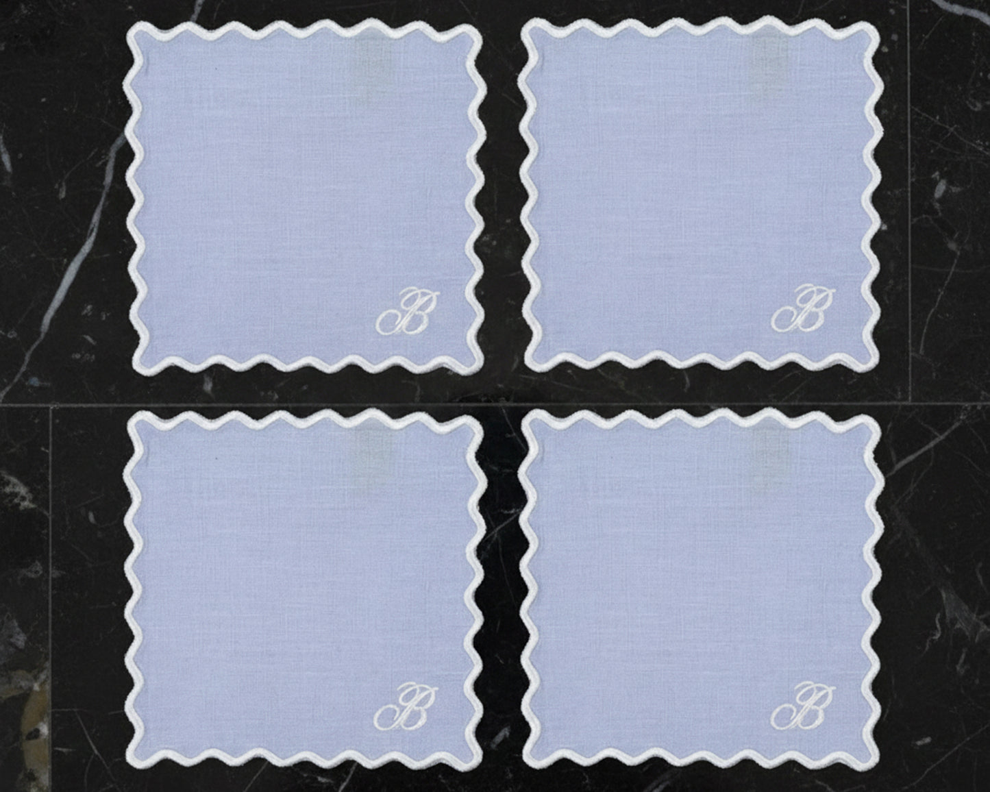 Four sky blue linen napkins with white wave borders featuring a large "B" monogram in the corner.