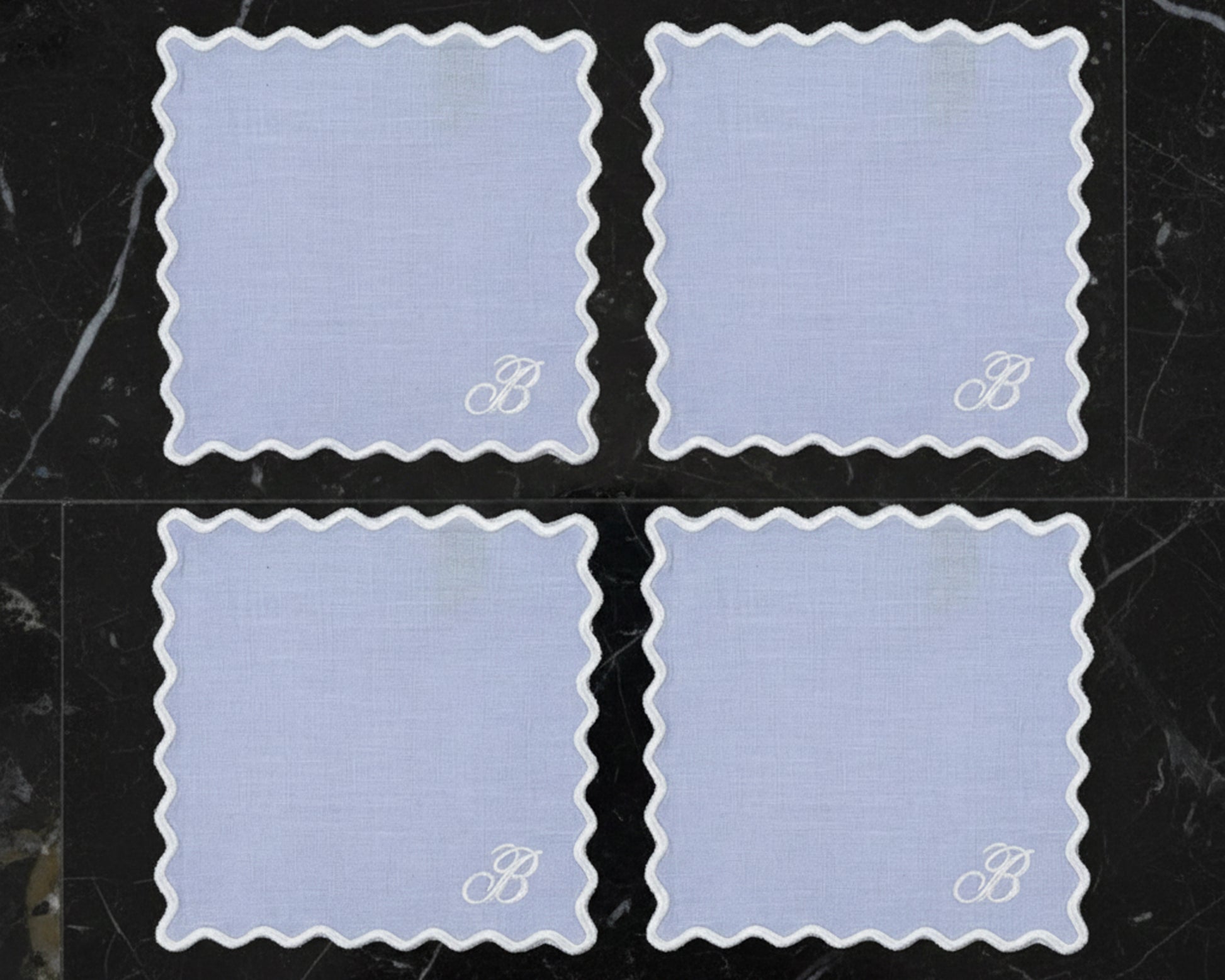 Four sky blue linen napkins with white wave borders featuring a large "B" monogram in the corner.