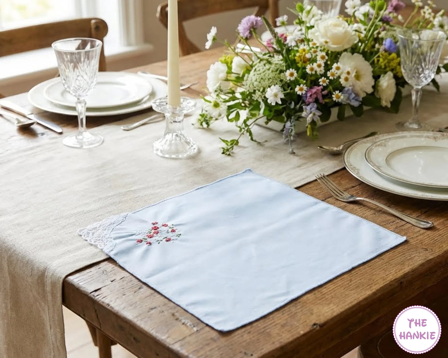 Dining table set with plates, glasses, and a floral centerpiece on a wooden table.