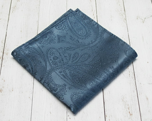 Single men's slate blue satin pocket square with an intricate jacquard paisley weave on a wood background.