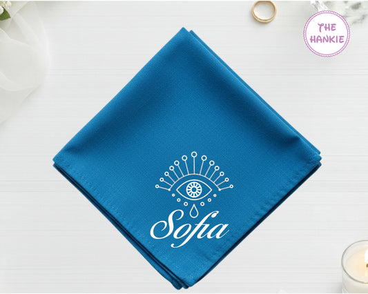A deep sapphire blue cotton pocket square featuring the name "Sofia" in white script below a white minimalist protective eye with star and droplet details.