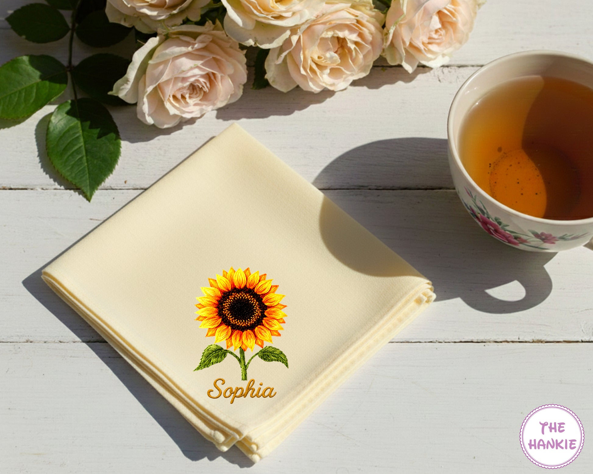A buttery yellow cotton handkerchief featuring the name "Sophia" and a detailed, radiant yellow and orange embroidered sunflower.