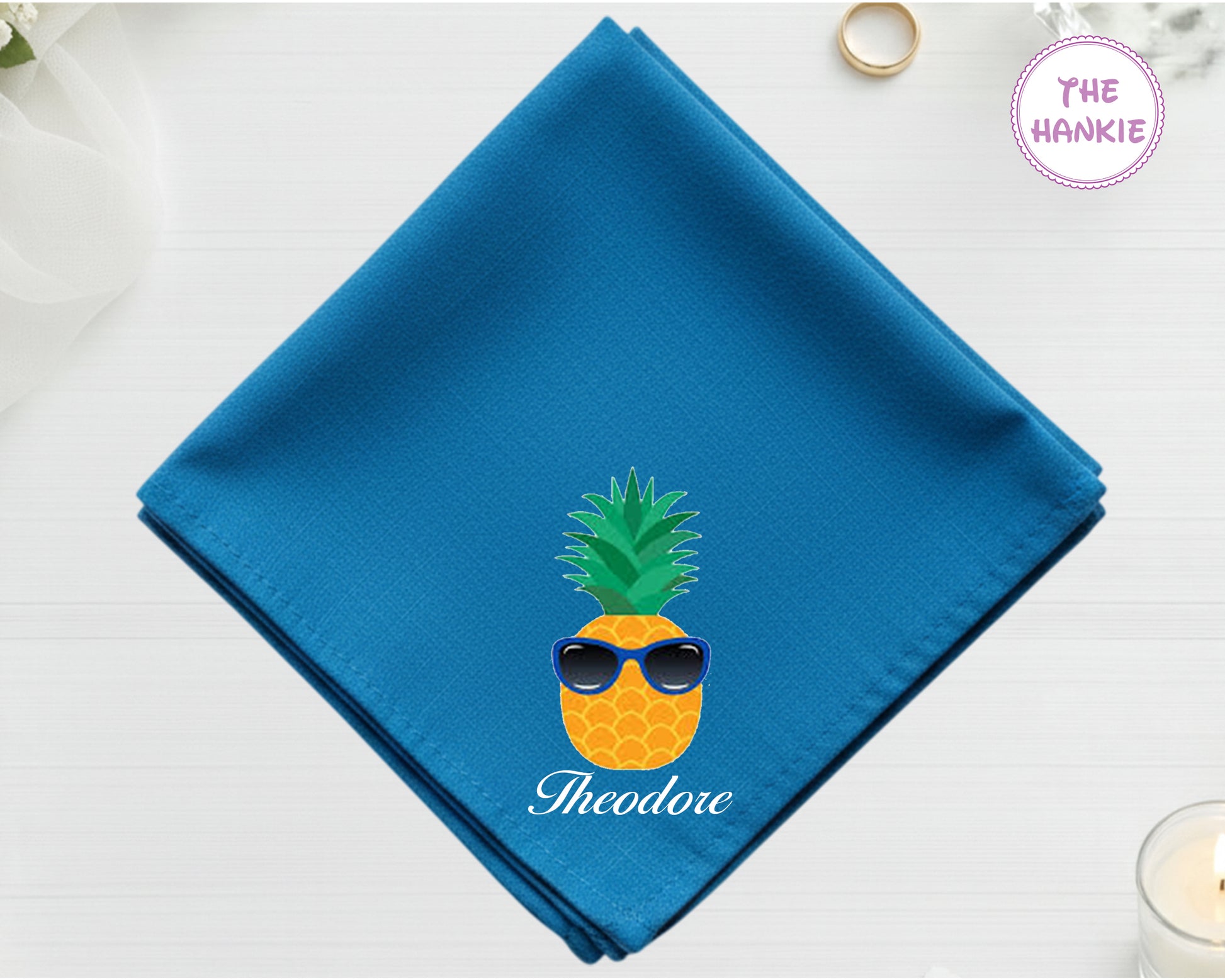 A deep sea blue cotton handkerchief personalized with "Theodore" below a pineapple wearing blue sunglasses.