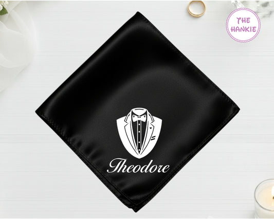 A midnight onyx black luxury satin handkerchief personalized with the name "Theodore" below a white vinyl print of a formal tuxedo shield icon.