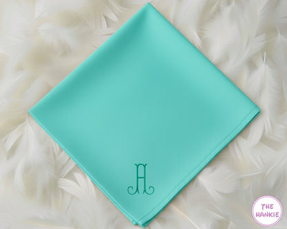 A vibrant turquoise cotton handkerchief with a clean, modern embroidered initial "A" featuring decorative serif flourishes in a matching teal thread.