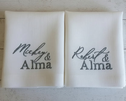 Two white pillows with embroidered names on a wooden surface