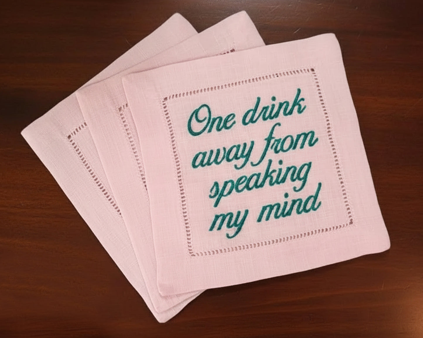 A group of colorful scalloped-edge linen napkins in rose pink, sky blue, and white with custom bar name embroidery.