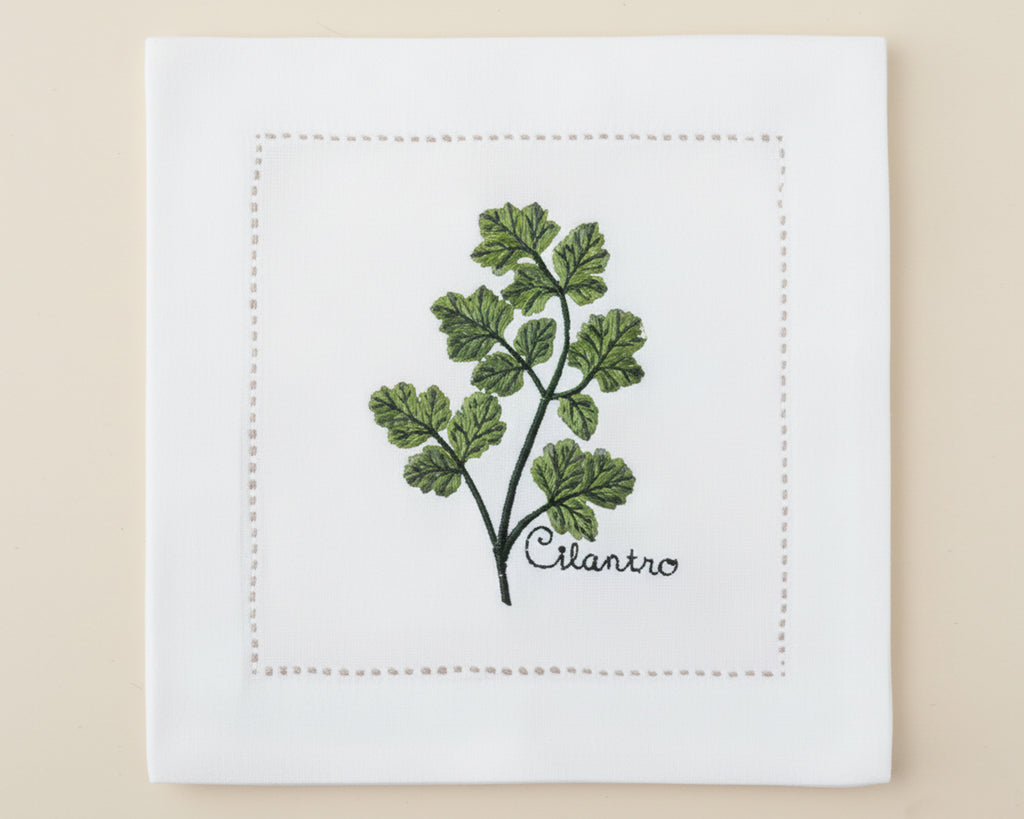 Single white linen cocktail napkin featuring a detailed green Basil branch embroidery with a delicate hemstitch border.