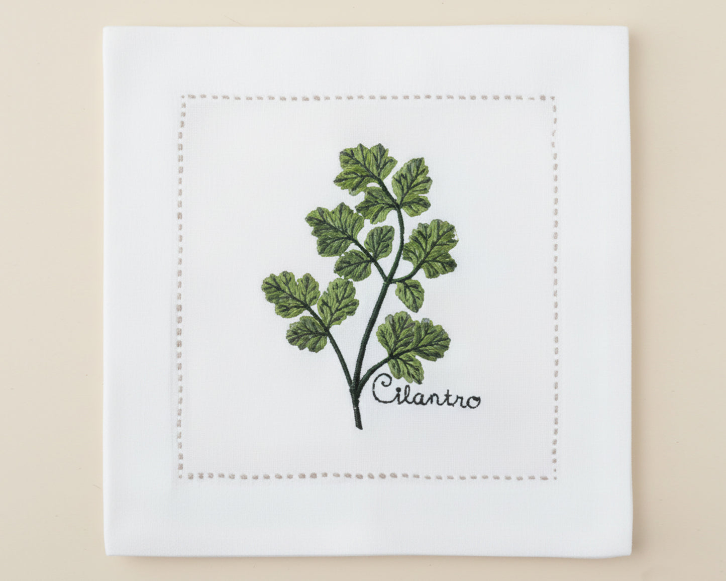 Single white linen cocktail napkin featuring a detailed green Basil branch embroidery with a delicate hemstitch border.