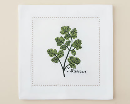 Single white linen cocktail napkin featuring a detailed green Basil branch embroidery with a delicate hemstitch border.