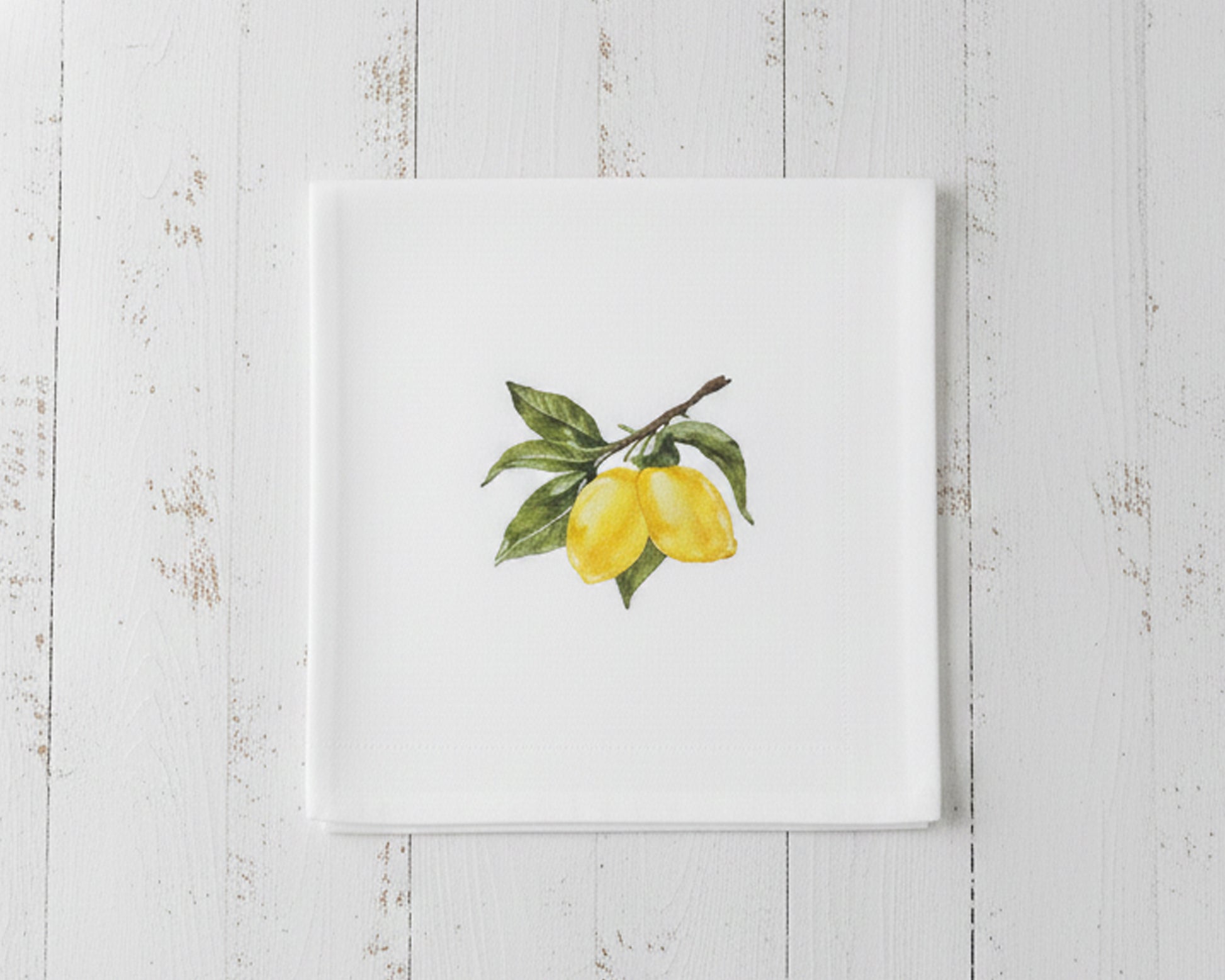 Close up of a single white linen cocktail napkin featuring a sun-ripened yellow lemon botanical embroidery centered on a crisp white fabric.
