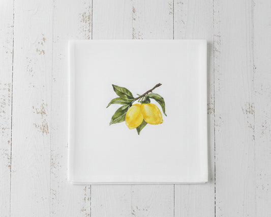Close up of a single white linen cocktail napkin featuring a sun-ripened yellow lemon botanical embroidery centered on a crisp white fabric.
