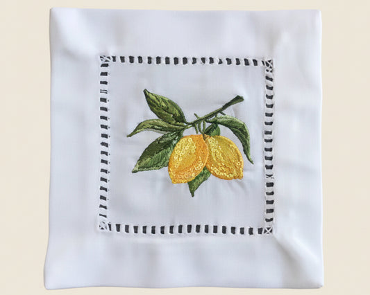Close up of a single 100% cotton cocktail napkin featuring a sun-ripened yellow lemon botanical embroidery centered on a crisp white fabric.
