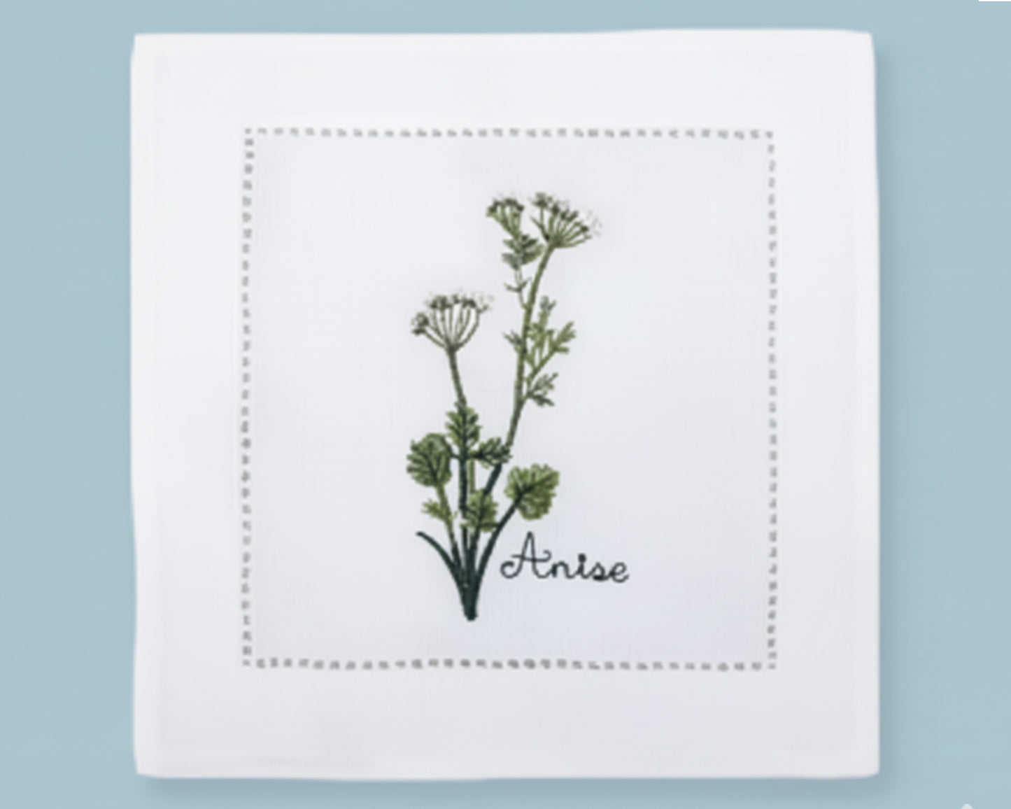 Single white linen cocktail napkin featuring a detailed yellow Dill flower embroidery and a decorative hemstitch perimeter.