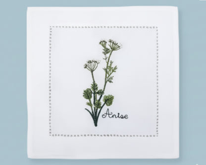 Single white linen cocktail napkin featuring a detailed yellow Dill flower embroidery and a decorative hemstitch perimeter.