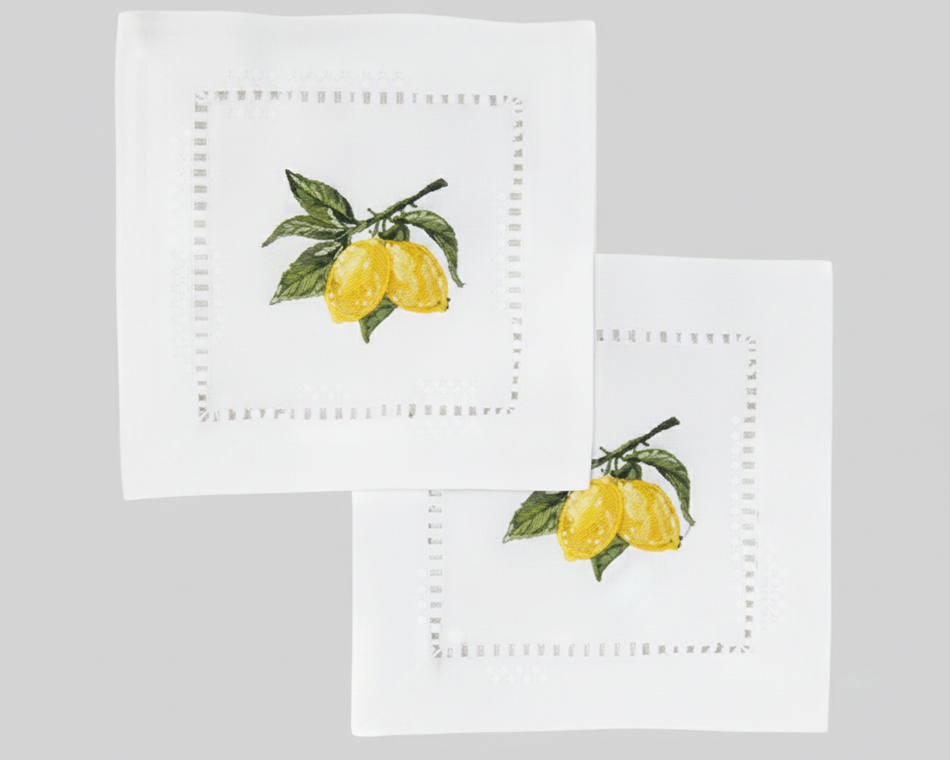 A fanned-out stack of VOICI lemon embroidered pure cotton napkins displayed on a light green background for modern bar styling.