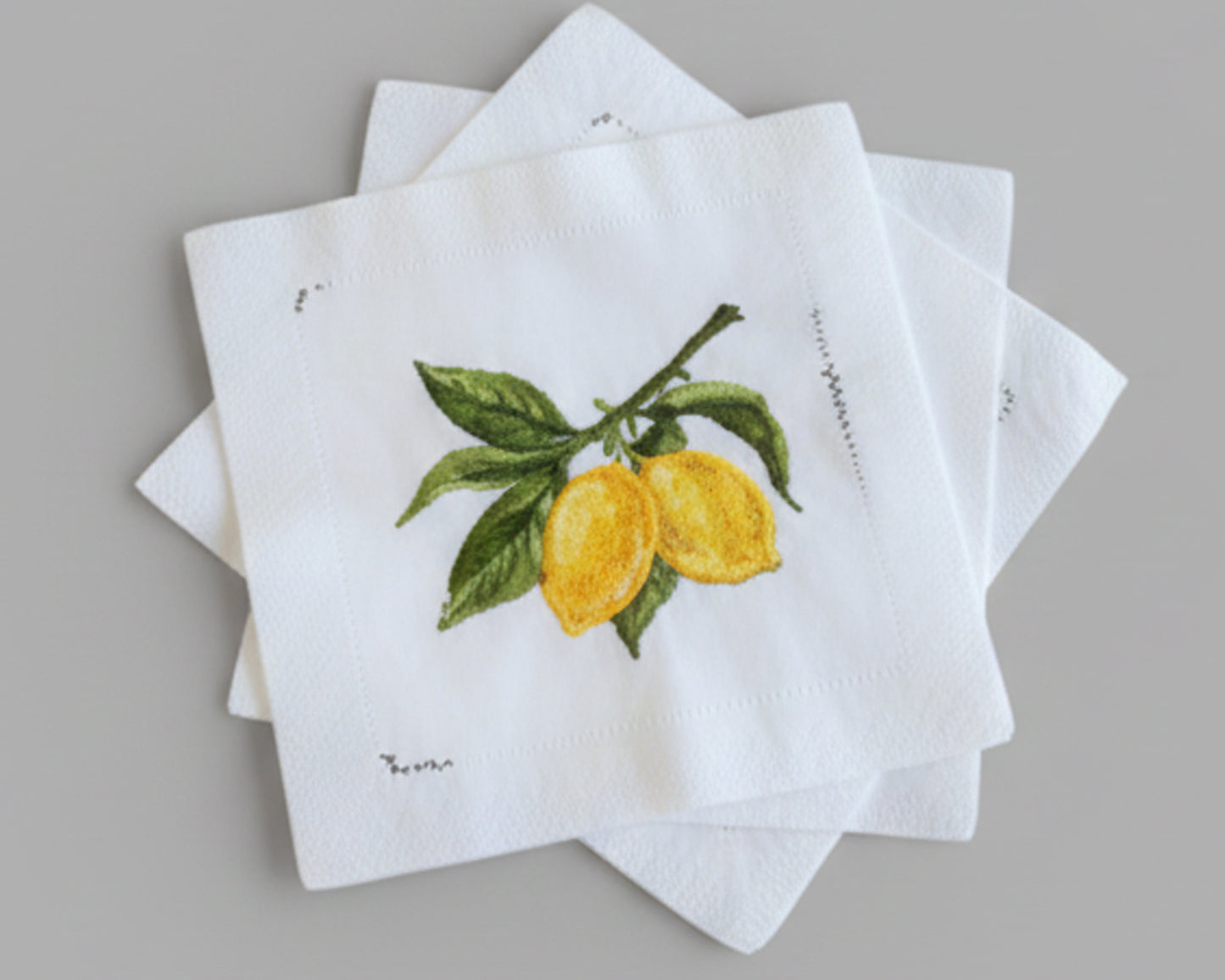 A decorative star-shaped stack of four white linen cocktail napkins showcasing detailed lemon citrus embroidery for high-end table decor.