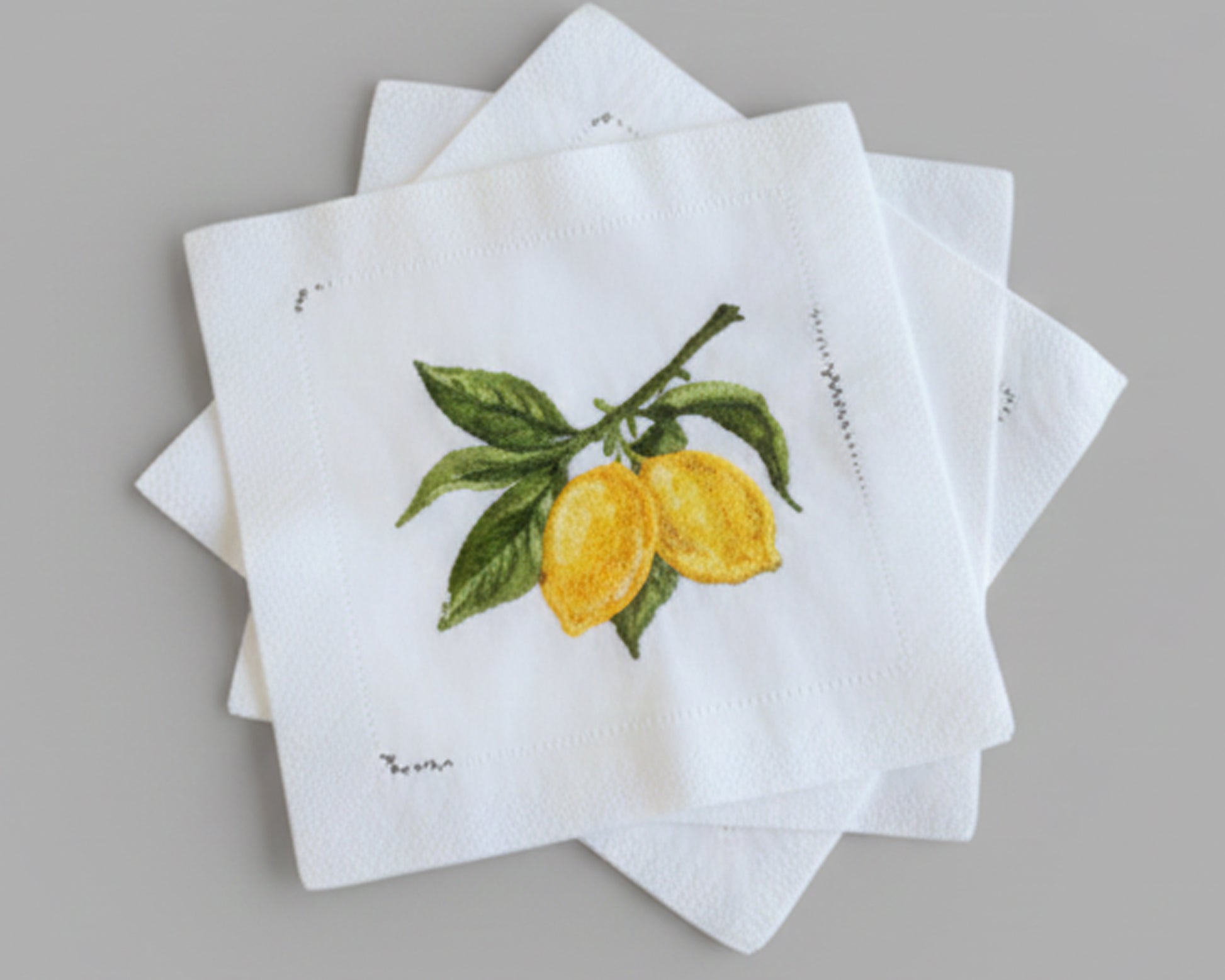 A decorative star-shaped stack of four white linen cocktail napkins showcasing detailed lemon citrus embroidery for high-end table decor.
