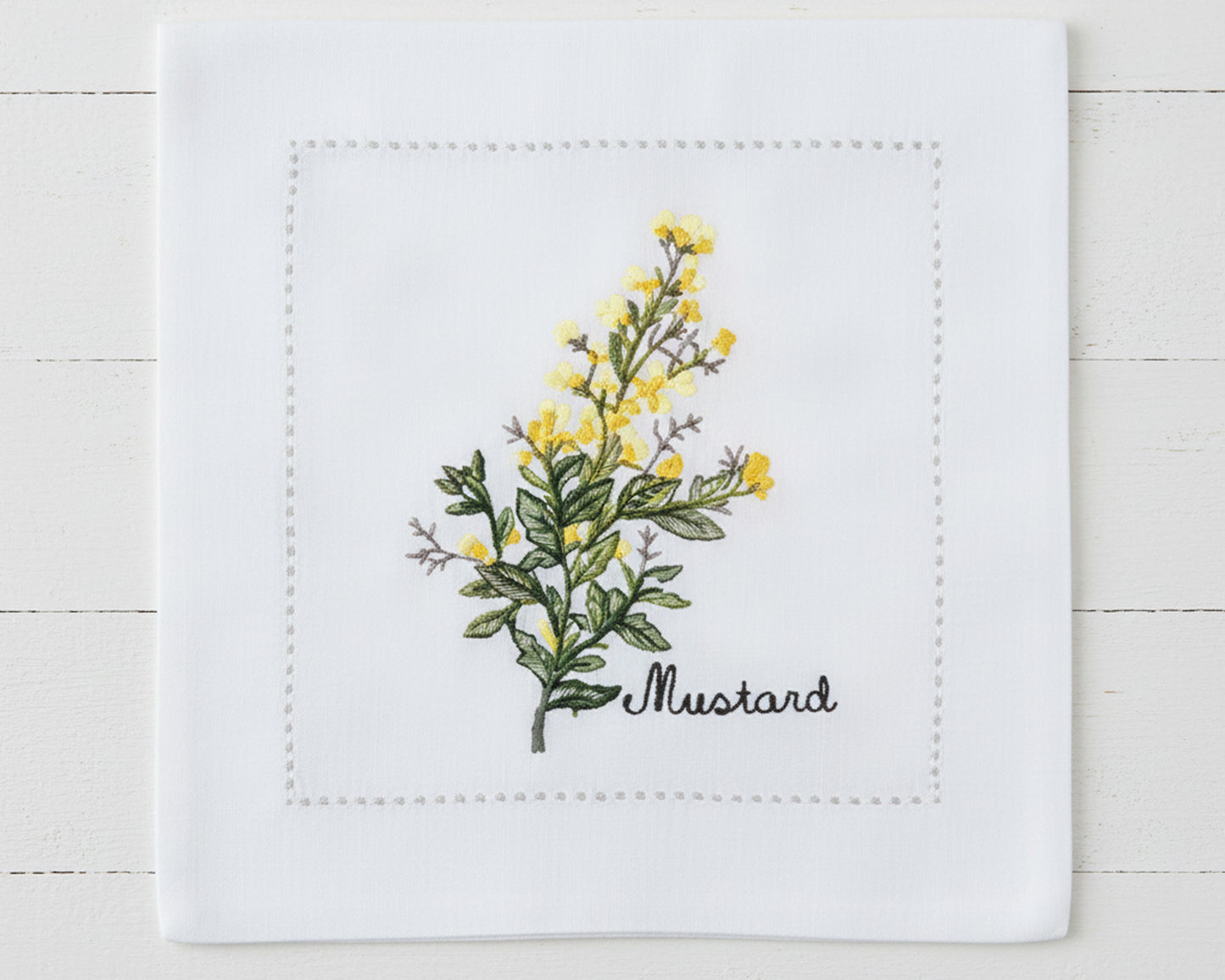 Single white linen cocktail napkin featuring detailed yellow Mustard flower embroidery and a tailored hemstitch border.