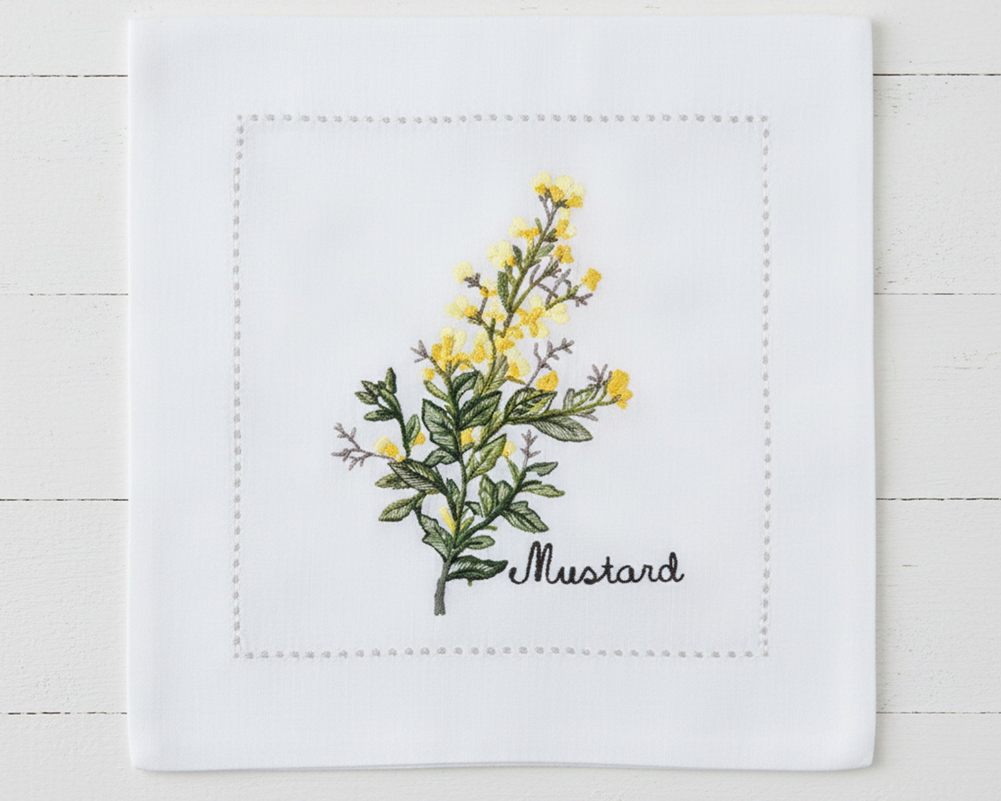 Single white linen cocktail napkin featuring detailed yellow Mustard flower embroidery and a tailored hemstitch border.