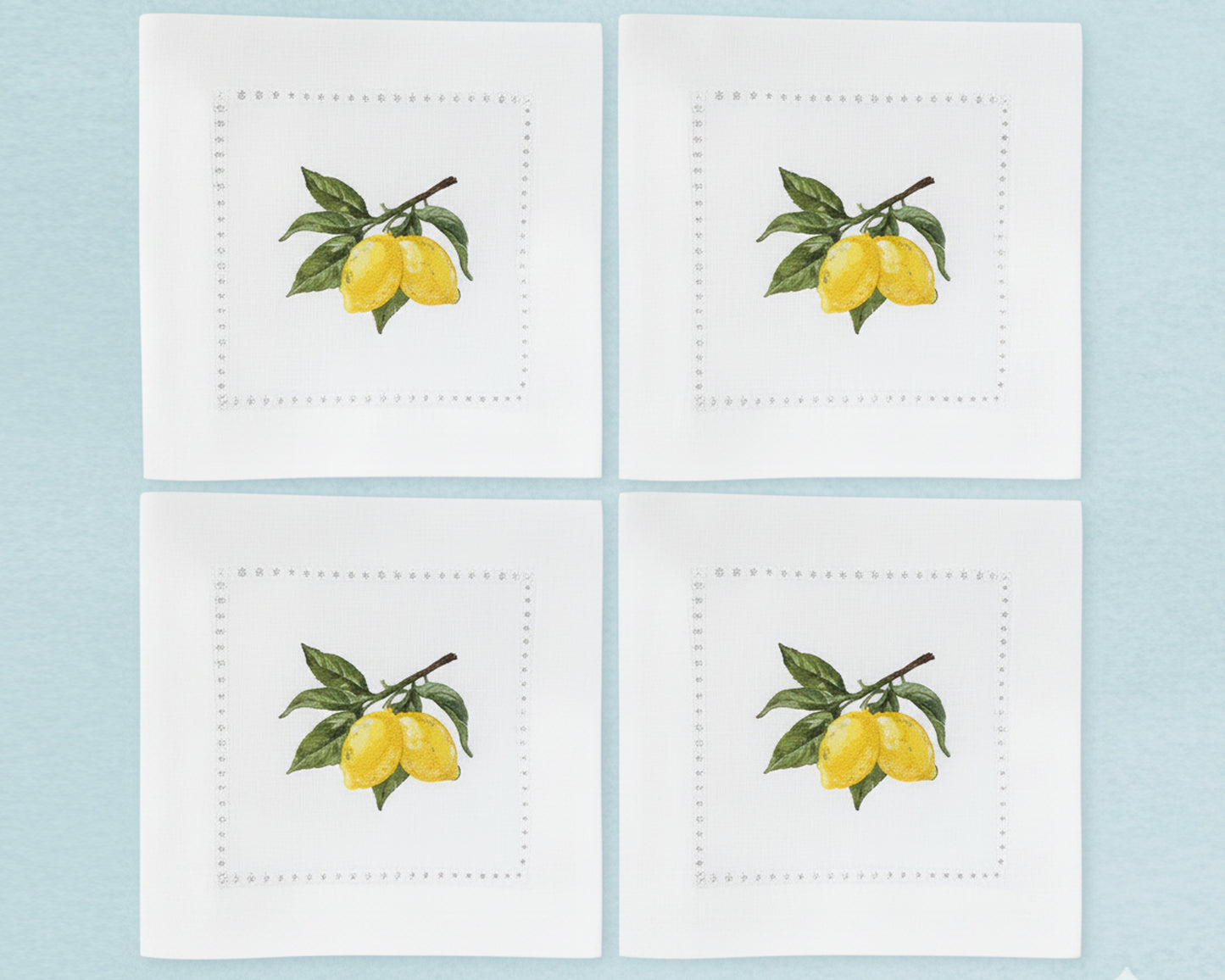 A set of six pure white cotton cocktail napkins featuring detailed yellow lemon and green leaf branch embroidery with a hemstitch border.