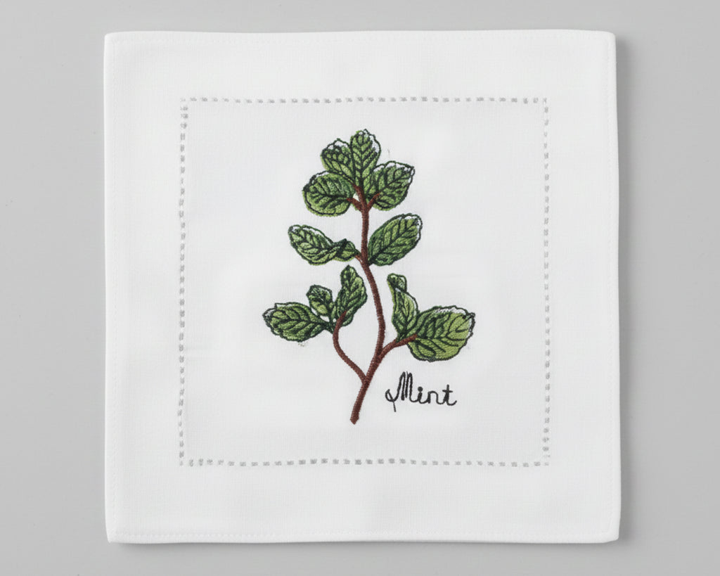 Single white linen cocktail napkin featuring a detailed purple-flowered Rosemary sprig embroidery with a hemstitch border.