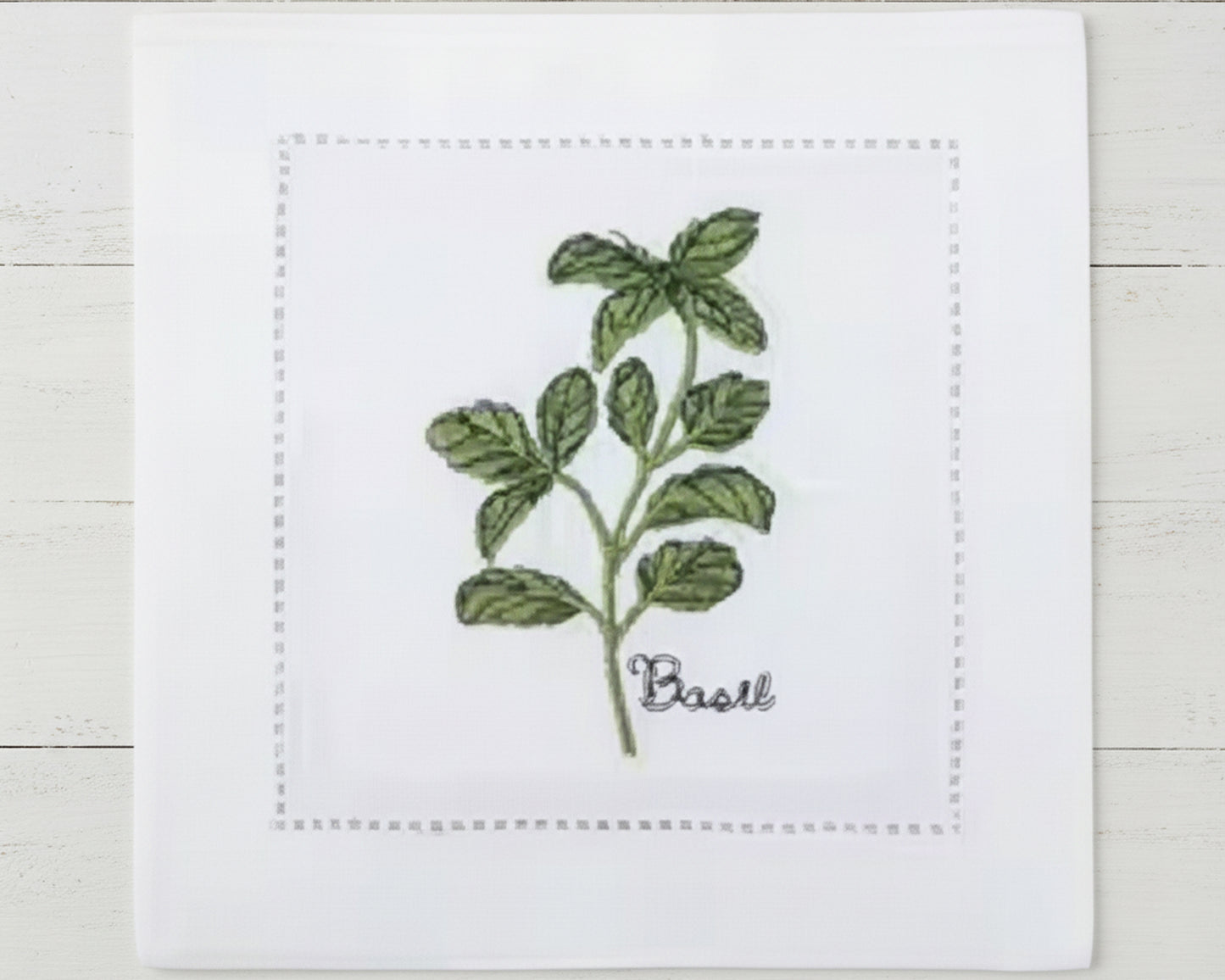 Single white linen cocktail napkin featuring a slender green Tarragon sprig embroidery with a hemstitch border on white linen.