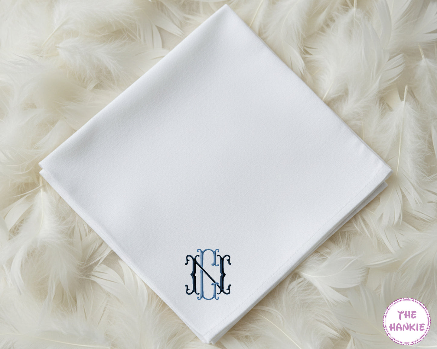 A classic white cotton handkerchief personalized with a sophisticated interlocking navy blue script monogram in the corner.