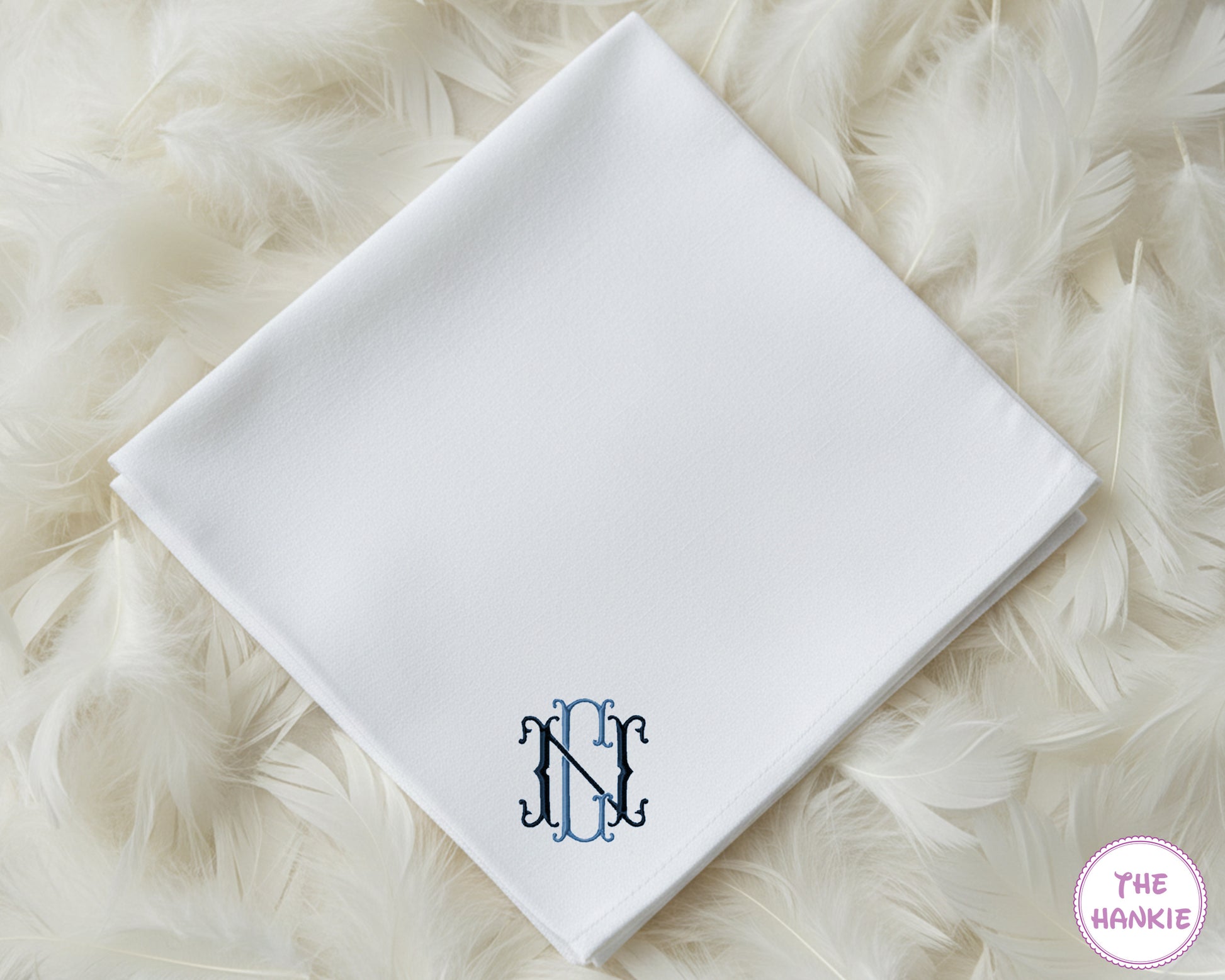 A classic white cotton handkerchief personalized with a sophisticated interlocking navy blue script monogram in the corner.