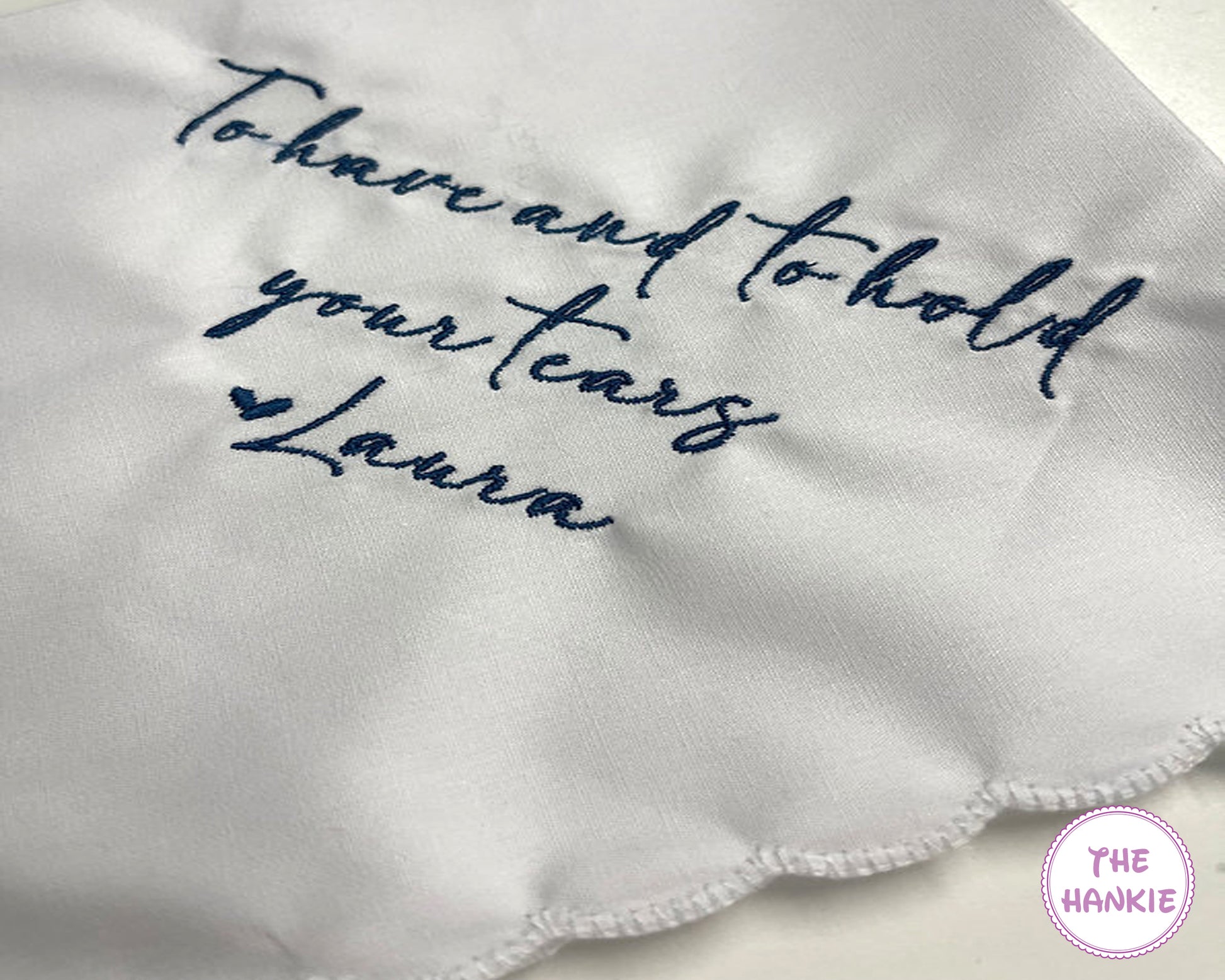 Embroidered hankie with 'To have and to hold your tears' and 'Laura' text on a white background.