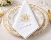 Elegant table setting with gold rimmed plates, white napkin with monogram, and gold cutlery.