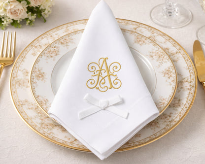 Elegant table setting with gold rimmed plates, white napkin with monogram, and gold cutlery.