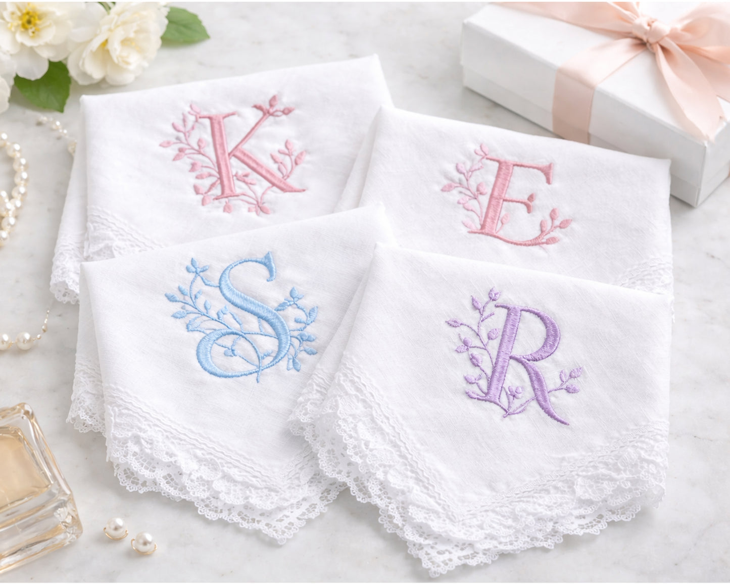 Set of white handkerchiefs with embroidered initials on a light surface.